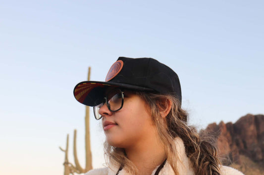 Black 5 panel hat with leather patch worn by woman outdoors