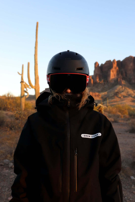 Person wearing black insulated snow jacket with helmet and goggles in desert landscape